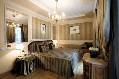 View of a bedroom at the Baglioni Hotel Carlton with a brown and grey colour scheme with a big double bed, mirro and chandelier 