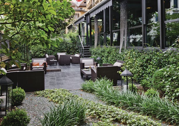 Terrace gardens at the Baglioni Hotel Carlton with trees and greenery and scattered cushioned chairs 
