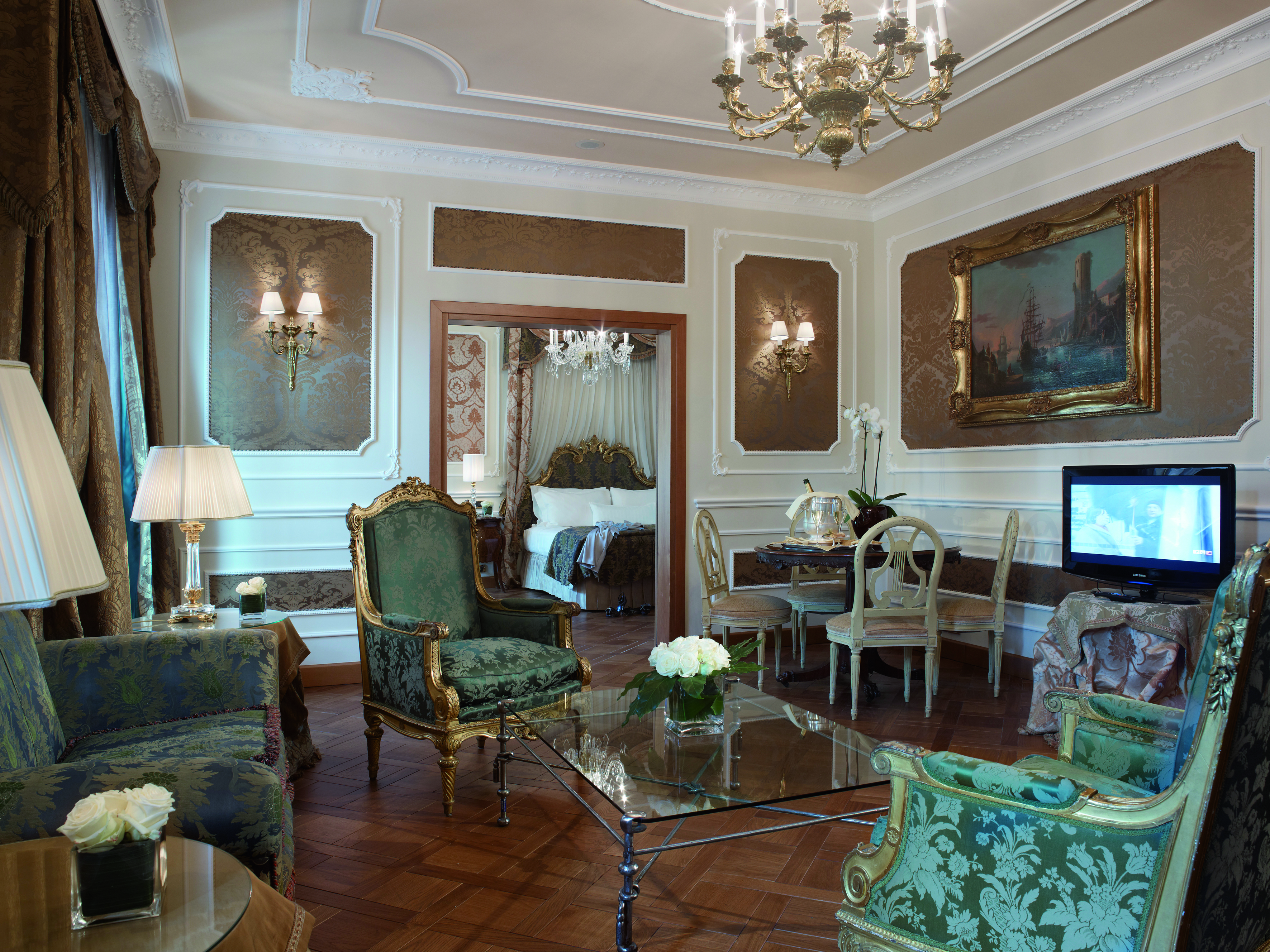 Presidential suite at the Baglioni Hotel Carlton with multiple chandeliers, floral arm chairs, a double bed and gold framed art on the walls