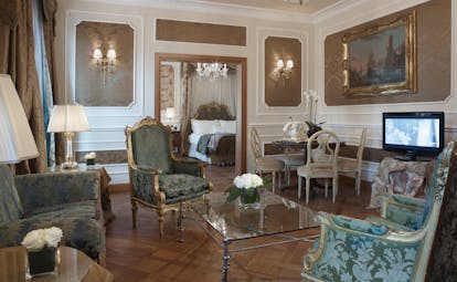 Presidential suite at the Baglioni Hotel Carlton with multiple chandeliers, floral arm chairs, a double bed and gold framed art on the walls