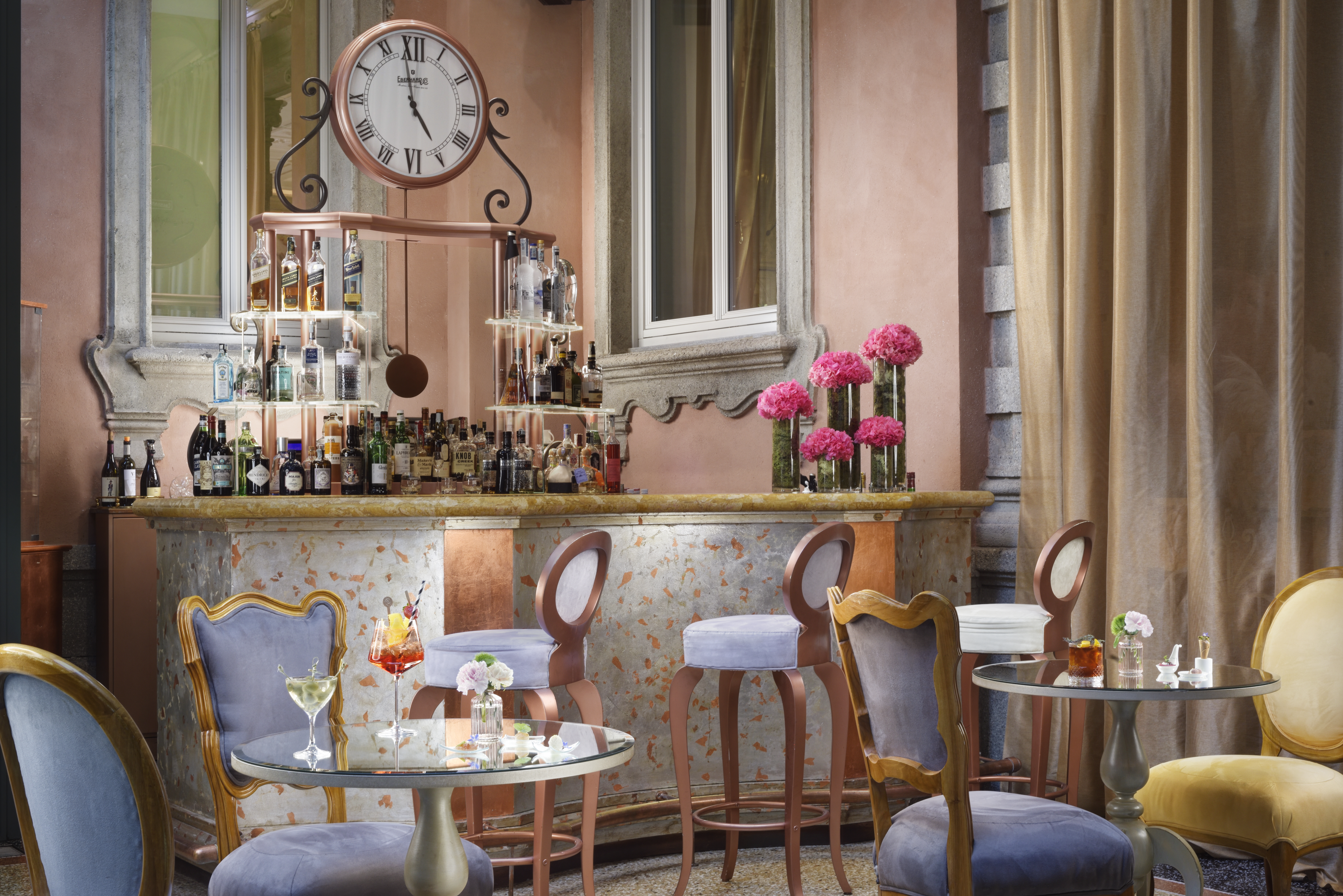 Chateau Monfort bar, with ornate clock face behind the bar, tall pale blue and wood stools, curved furnishings, and a fairytale vibe