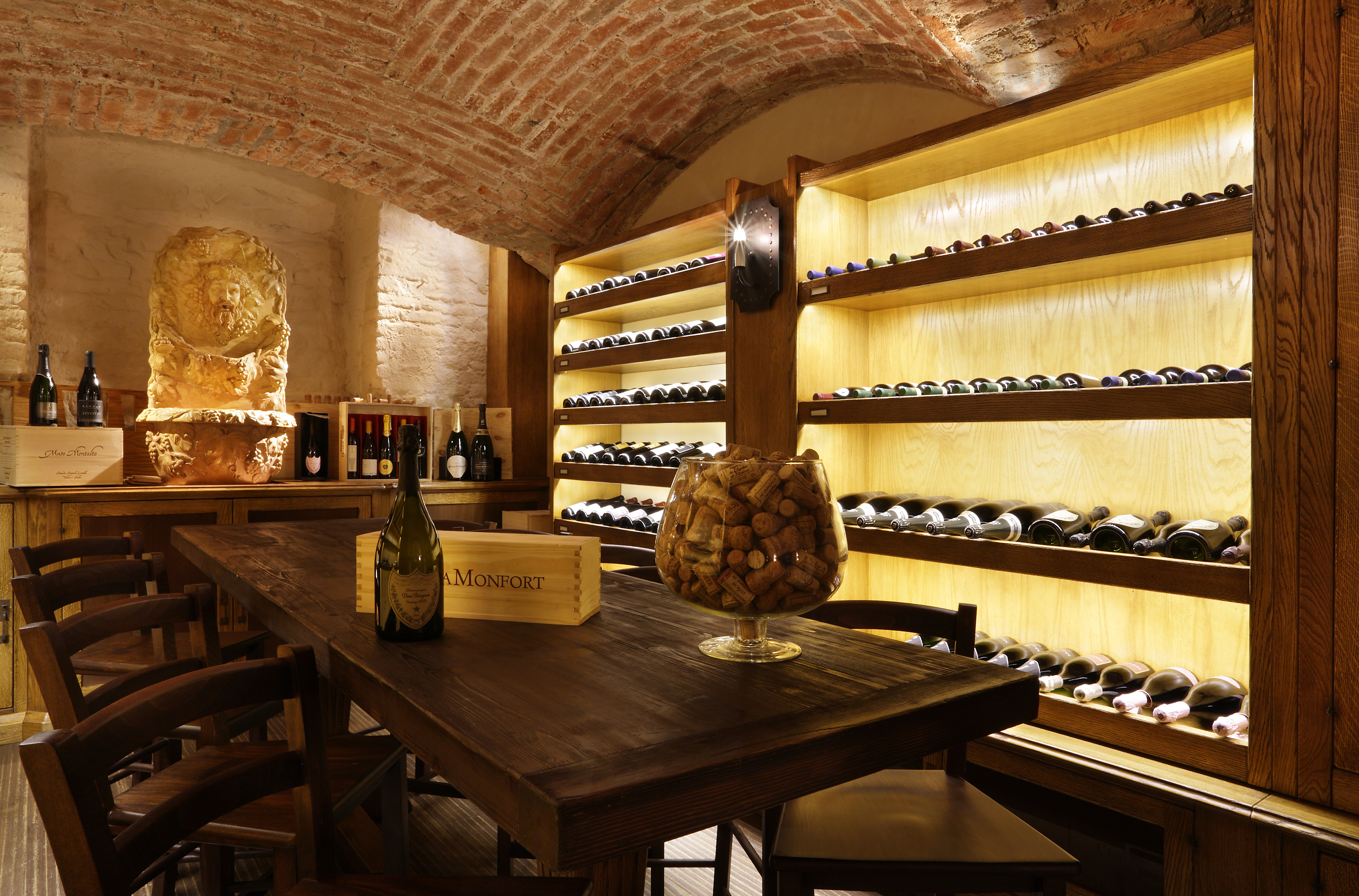 Chateau Monfort wine cellar, with curved brick ceiling, dark wooden table and chairs, and shelves of bottles