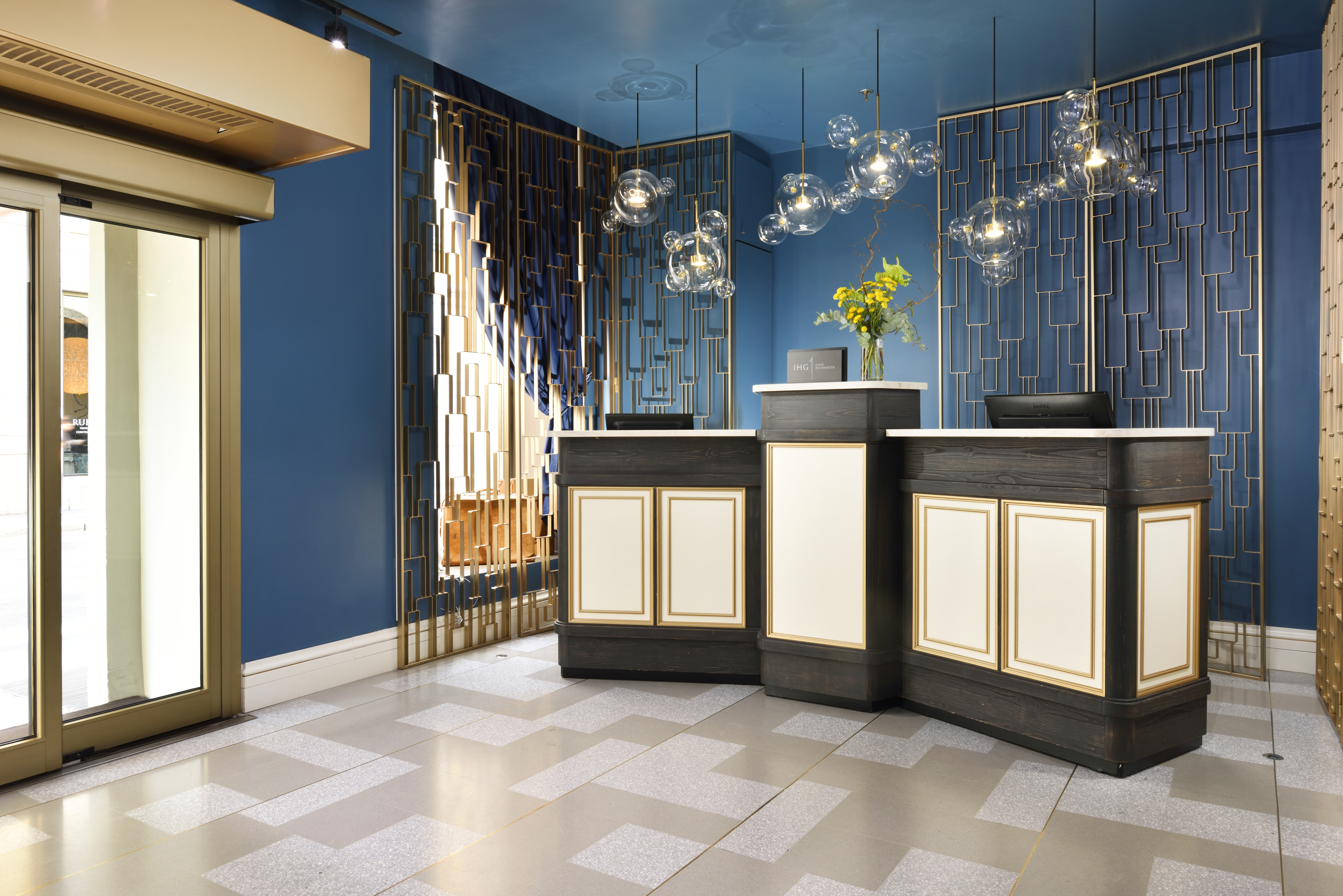 Hotel Indigo Milan reception, with dark teal walls, a sleek black and white desk, and white and gold floor tiles