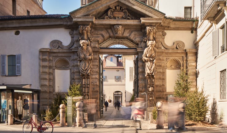 Hotel Portrait Milano entrance, with ornate stone arch, statues, and white-washed buildings