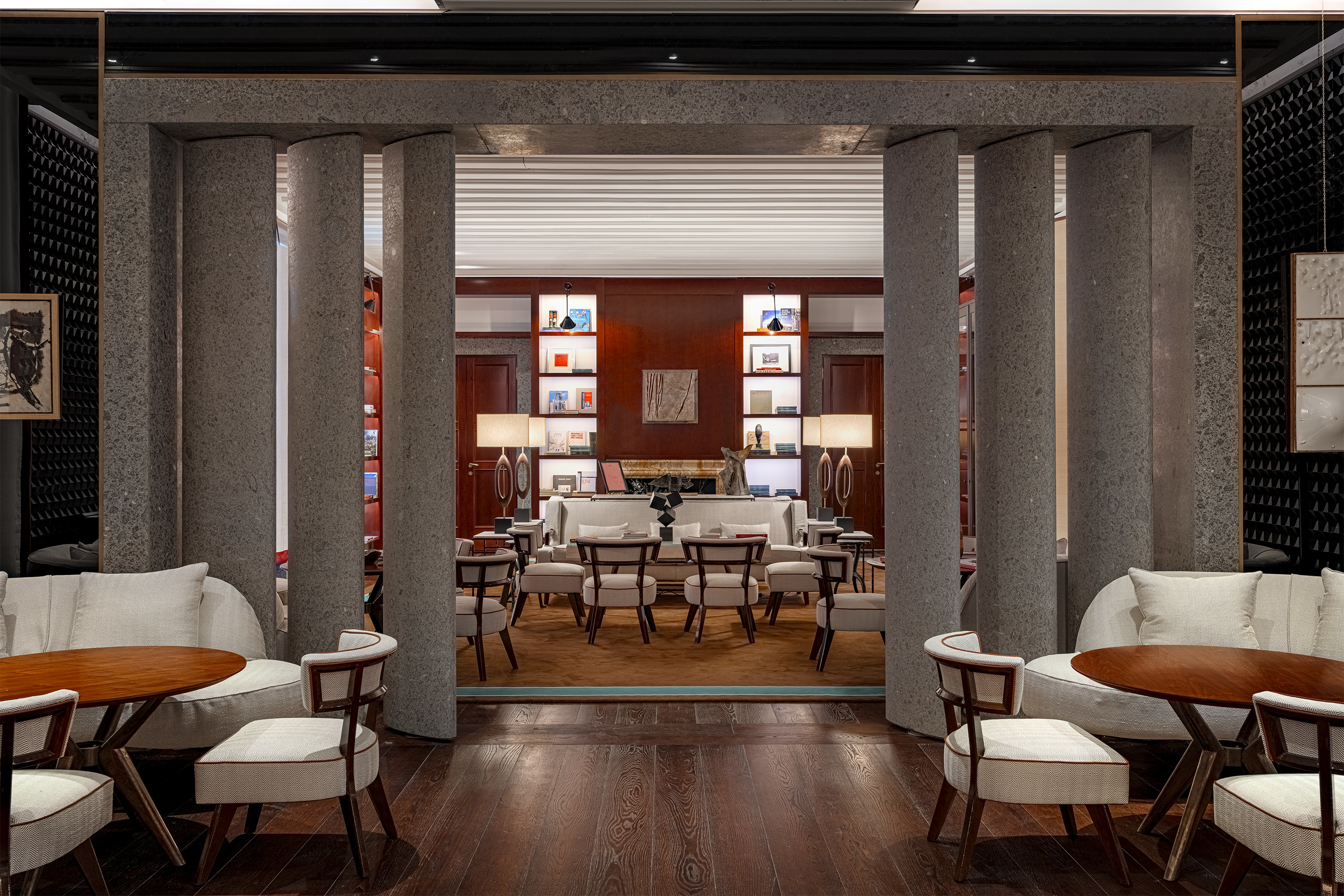 Hotel Portrait Milano library with white sofas and wooden tables, dark wood walls, and central concrete pillars