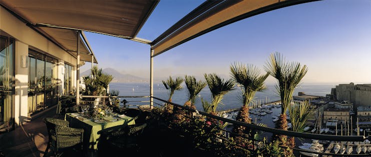 View of the roof garden at the Grand Hotel Vesuvio with palm trees on the roof and overlooking the city and the blue sea