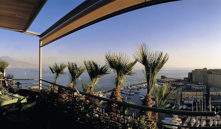 View of the roof garden at the Grand Hotel Vesuvio with palm trees on the roof and overlooking the city and the blue sea
