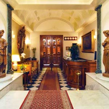 Hotel reception area with statues, a long red rug, high ceilings and paintings on the walls