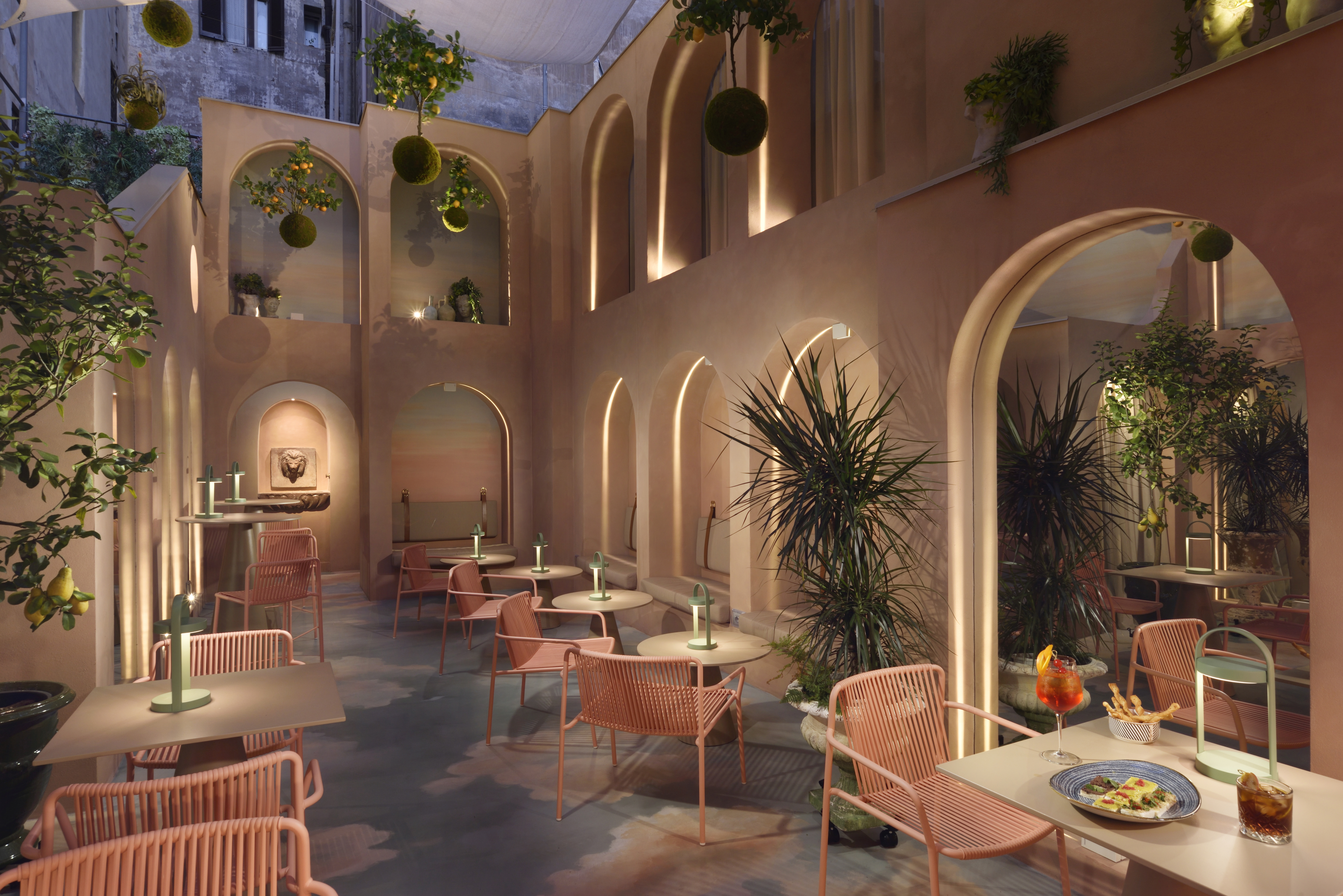 Leon's Place inner courtyard with ice cream pink walls with arcade arches, pink chairs and white tables, and hanging plants, with low soft lighting