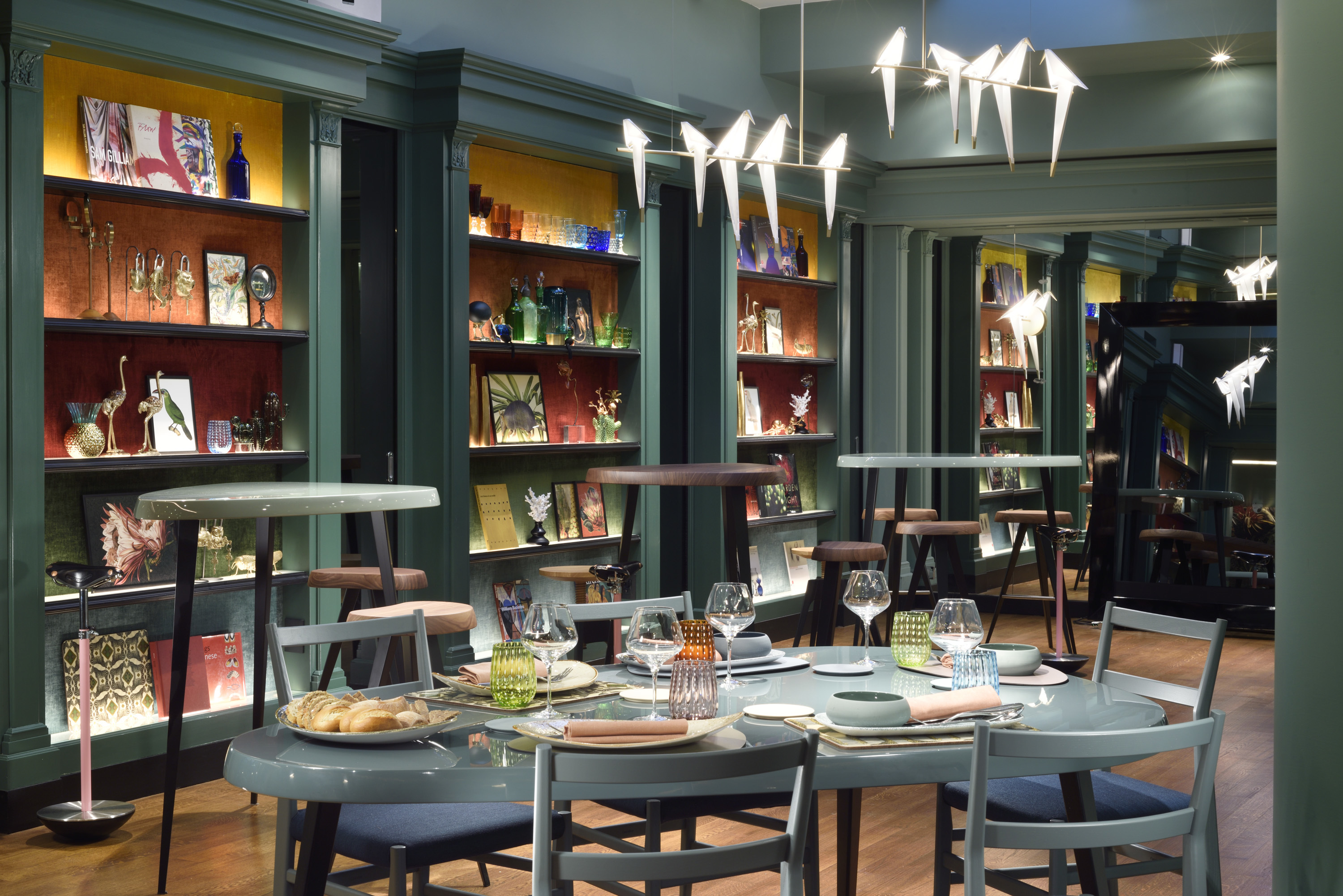 Leon's Place Ristorante Tavolo with teal walls, colourfully backed shelves, and table laden with plates and glasses, and unique lighting resembling birds sitting on a branch