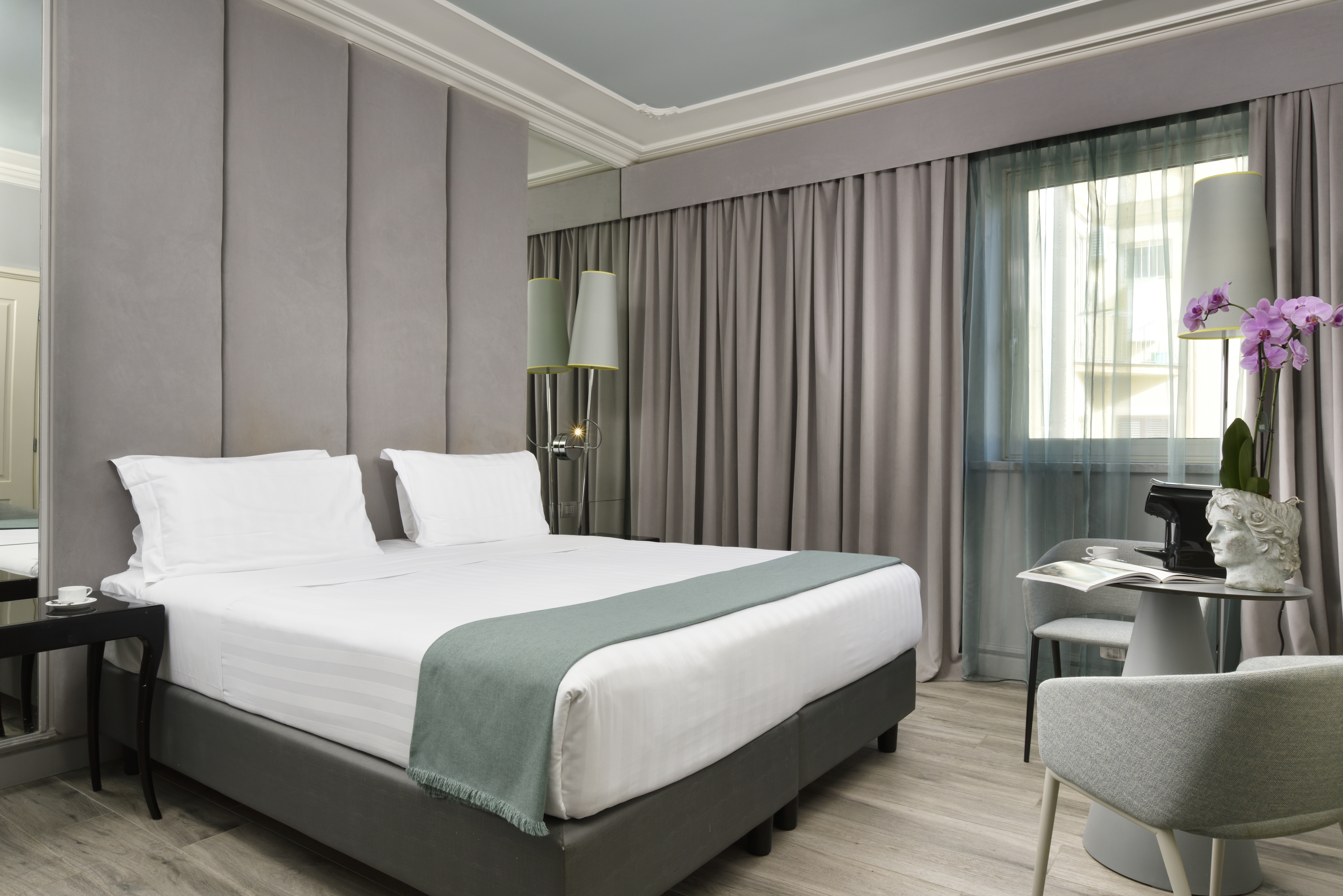 Leon's Place room with neutral grey, white, and teal colour palette, mirrored walls either side of the double bed, and a small table and chair