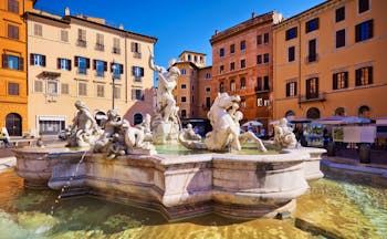 Baroque fountain of Neptune with water around and ochre houses at the Piazza Navona in Rome