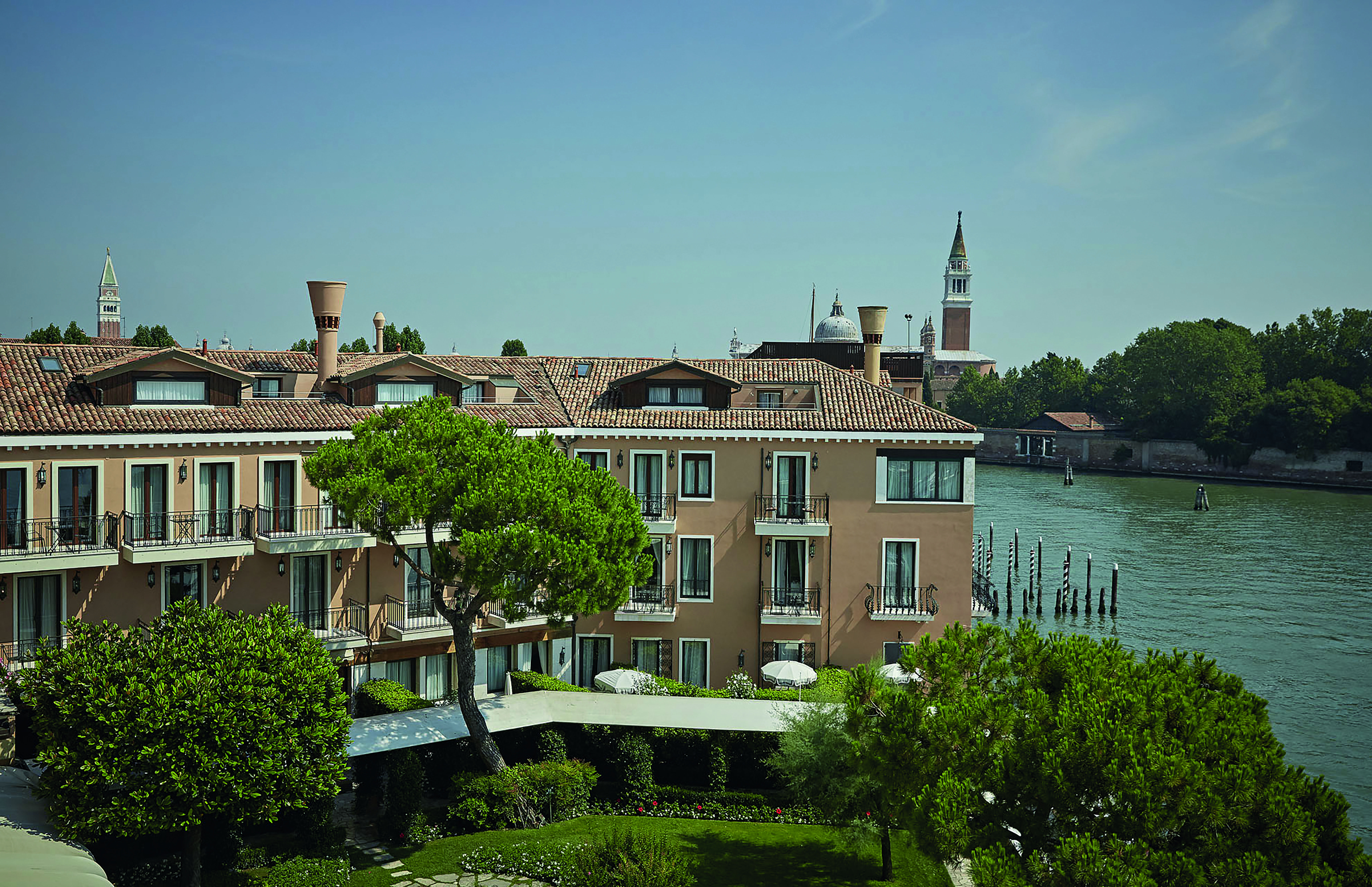 View of the exterior of the Belmond Hotel Cipriani with greenery infront of the hotel and water behind