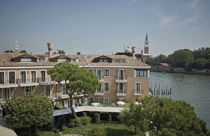 View of the exterior of the Belmond Hotel Cipriani with greenery infront of the hotel and water behind