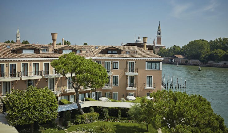 View of the exterior of the Belmond Hotel Cipriani with greenery infront of the hotel and water behind