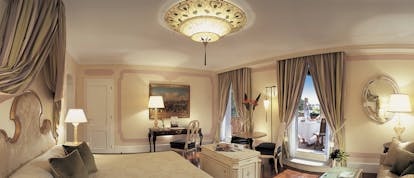 Belmond Hotel Cipriani cream and grey colour themed suite, with king sized bed, yellow lamp lighting and a chandelier