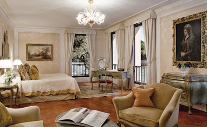 Belmond Hotel Cipriani suite with king sized bed, gold and cream colour scheme, a chandelier and big windows openinng up onto a balcony