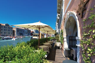Ca Sagredo Venice terrace outdoor seating area overlooking canal dining tables umbrellas