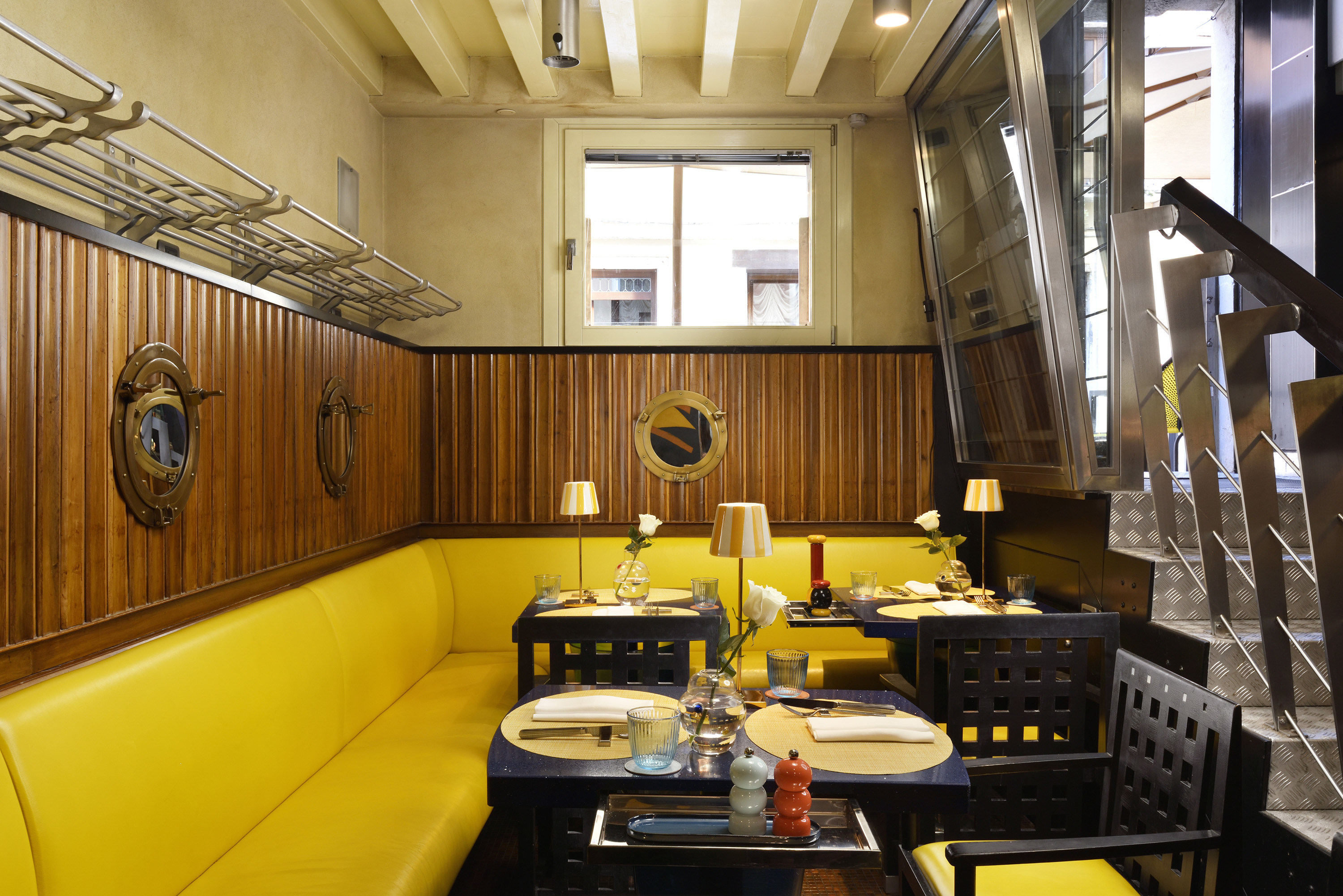 Ca' Pisani restaurant, with bright yellow corner booth, wooden panelled walls, and black chairs, set beside a glass wall