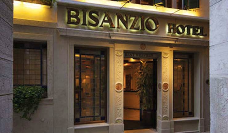 Entrance to the Bisanzio Hotel with the sign lit up in black above the wooden door