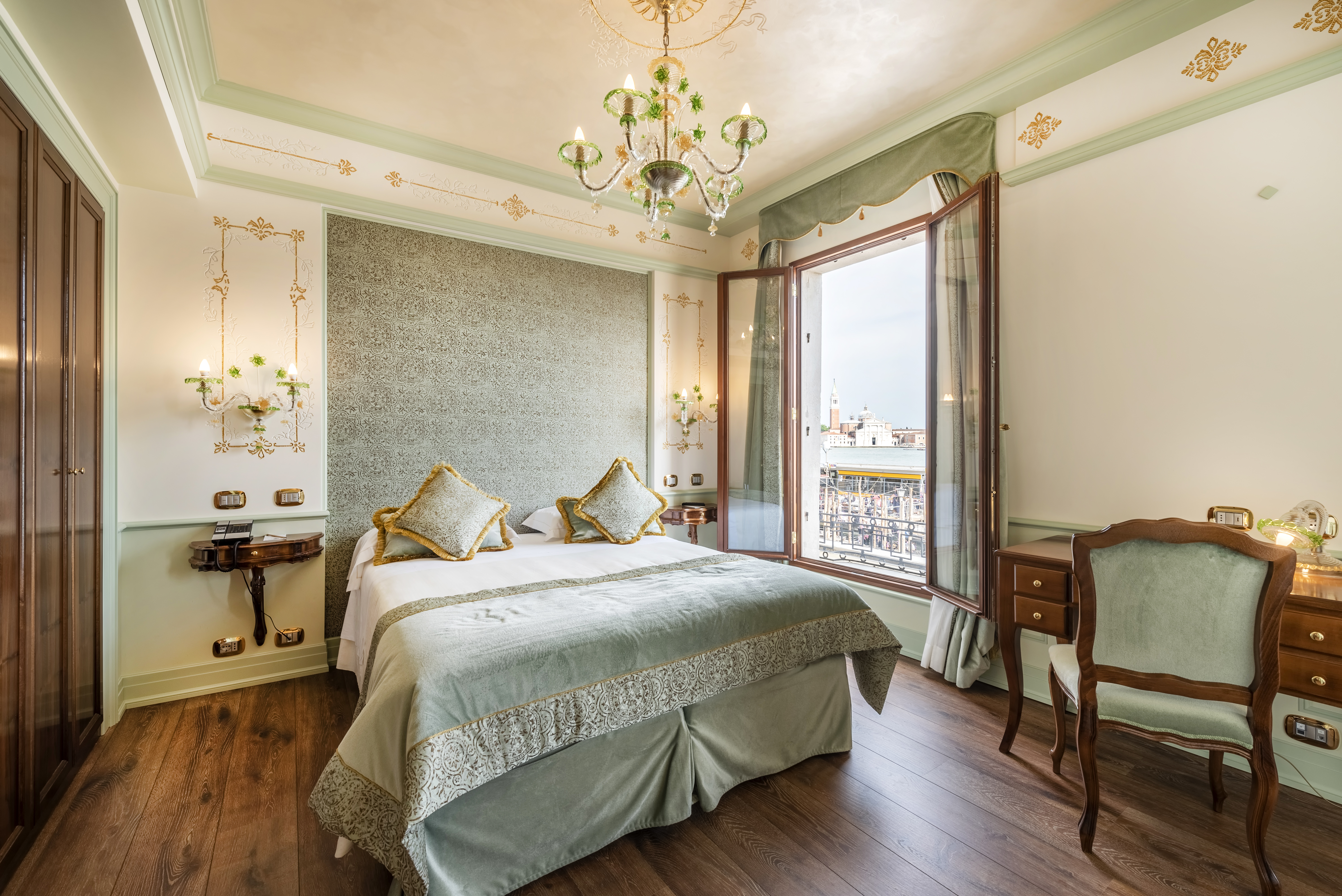 Hotel Monaco & Grand Canal Deluxe Room with pale green and gold decor, dark wood floor and wardrobe, and windows opening onto canal views