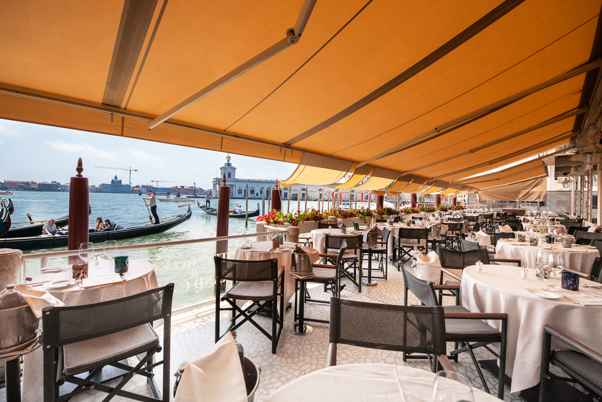 Hotel Monaco & Grand Canal restaurant terrace, with orange awning, canal and gondola views, and white-clothed tables with black chairs