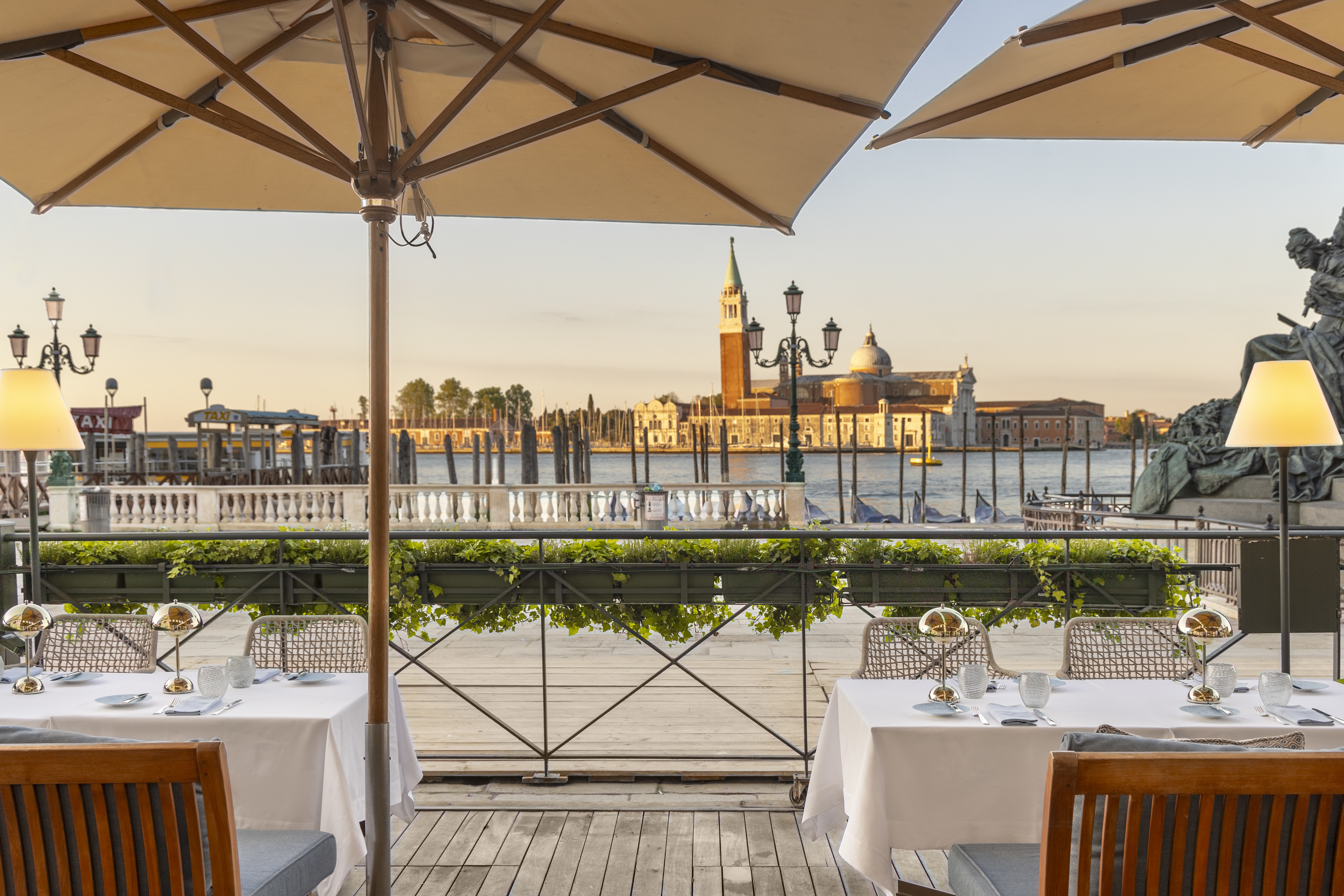Londra Palace Venezia restaurant terrace, with white-clothed tables, parasols, and stunning sunset view across the water to the San Giorgio Maggiore Abbey