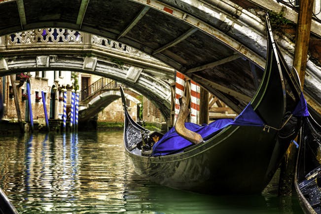 Gondola under low bridge in Venice with reflections on water