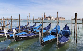 Row of gondolas with blue covers moored to posts opposite San Giorgio Maggiore Venice