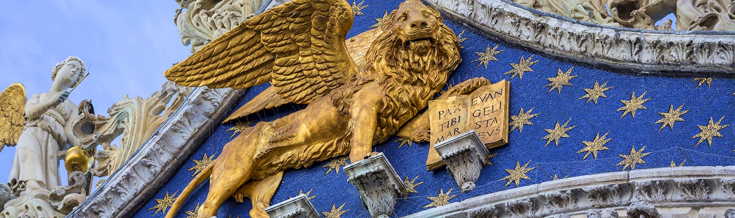 Golden lion statue on front of ornate blue and golden starred facade in Venice