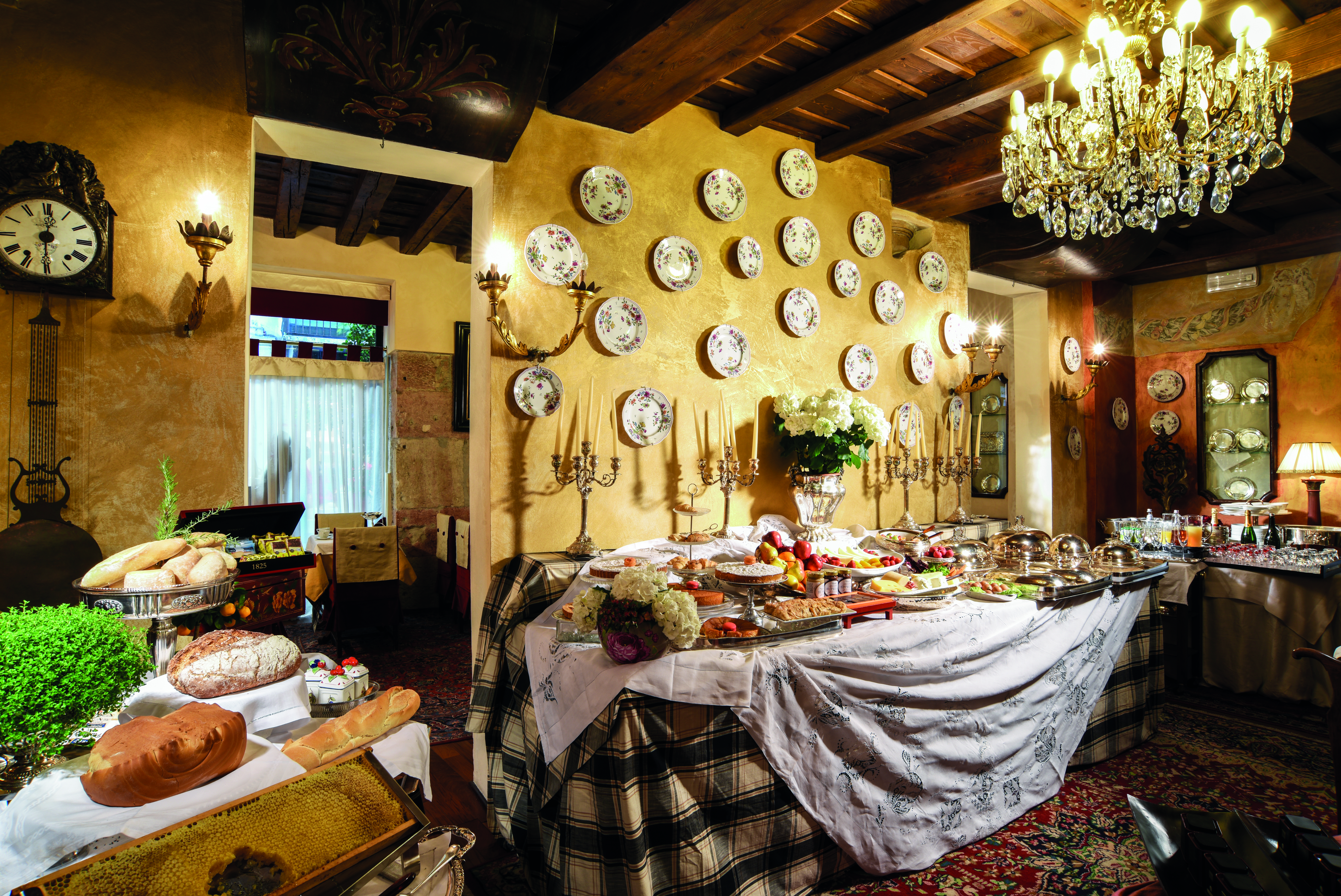 Breakfast buffet spread with large chandelier hanging from ceiling, wood pannelled ceilings and food laid out on top of table cloth