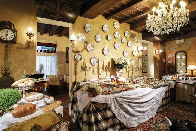 Breakfast buffet spread with large chandelier hanging from ceiling, wood pannelled ceilings and food laid out on top of table cloth