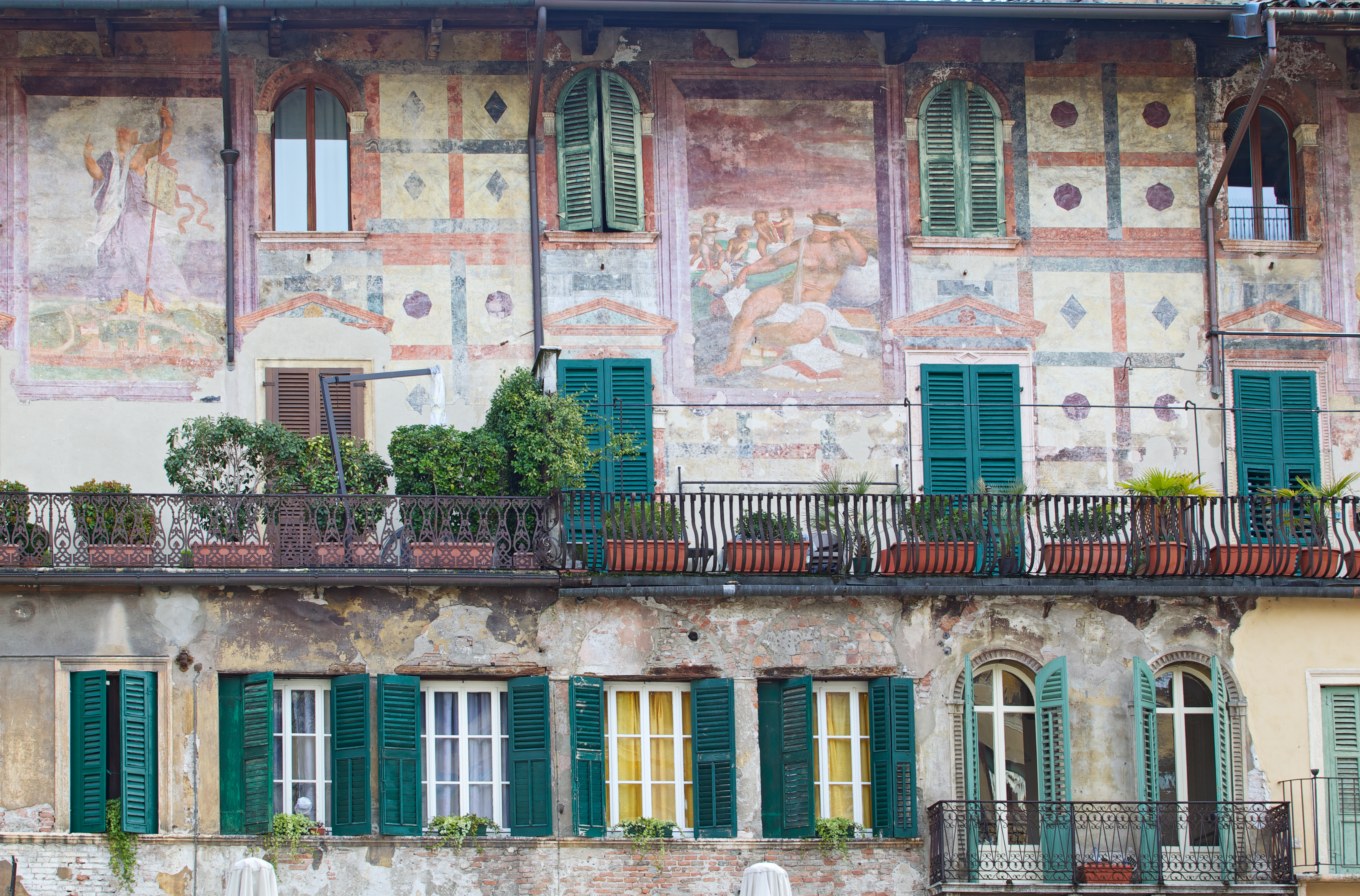 Ornate murals in pink and green on wall of old building with green shutters in Piazza delle Erbe Verona