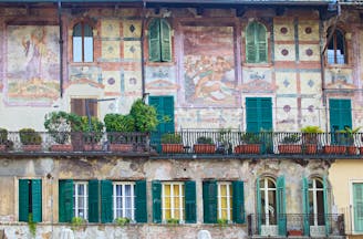Ornate murals in pink and green on wall of old building with green shutters in Piazza delle Erbe Verona