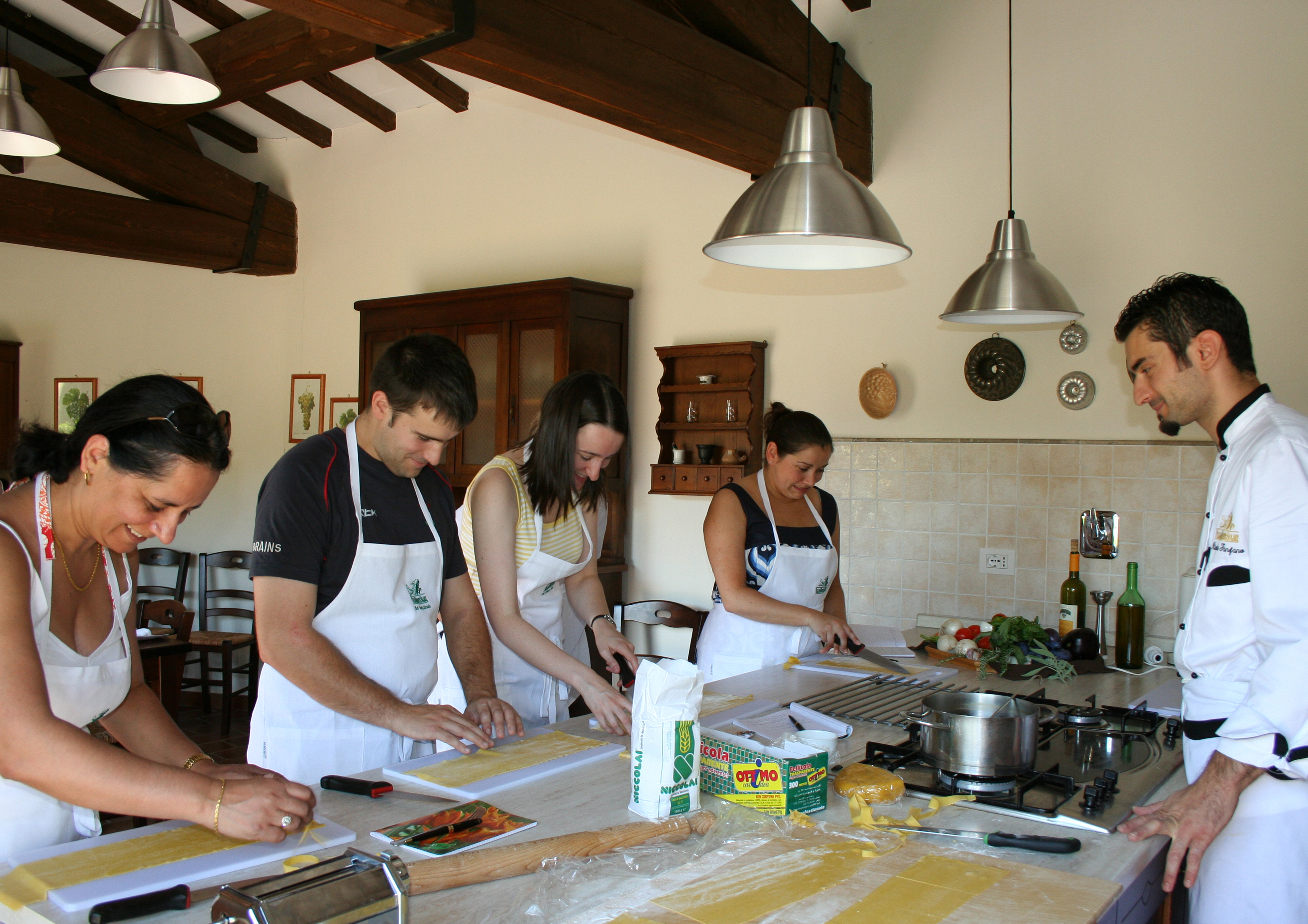 People in kitchen standing at table preparing food with chef watching