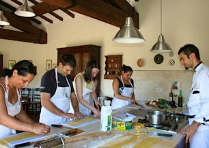 People in kitchen standing at table preparing food with chef watching