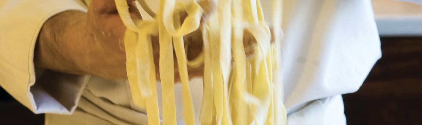 Chef in whites holding strands of freshly made tagliolini