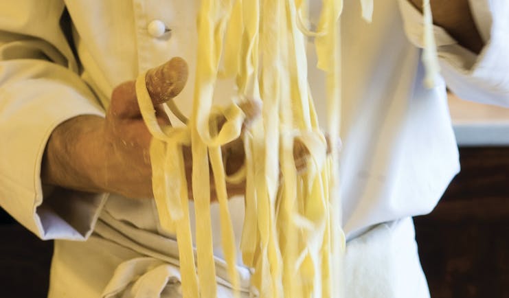 Chef in whites holding strands of freshly made tagliolini
