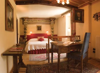 Bedroom with large double bed, desk, chair and paintings on the walls