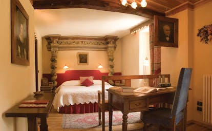 Bedroom with large double bed, desk, chair and paintings on the walls