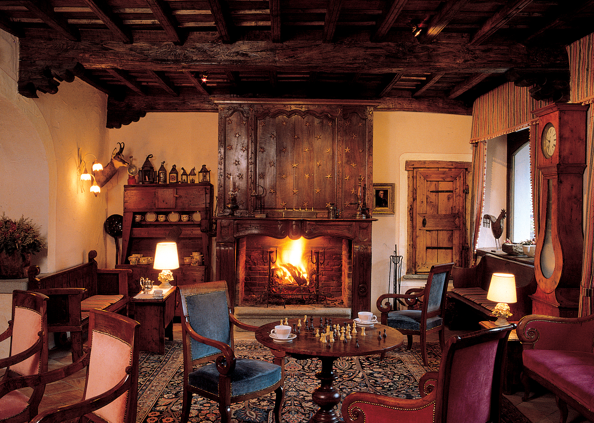 Cosy indoor lounge area with fire place, arm chairs, chess board on the table and old fashioned wooden deocrations