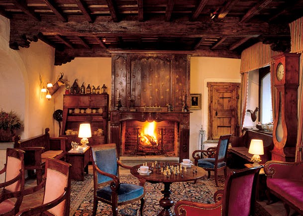 Cosy indoor lounge area with fire place, arm chairs, chess board on the table and old fashioned wooden deocrations