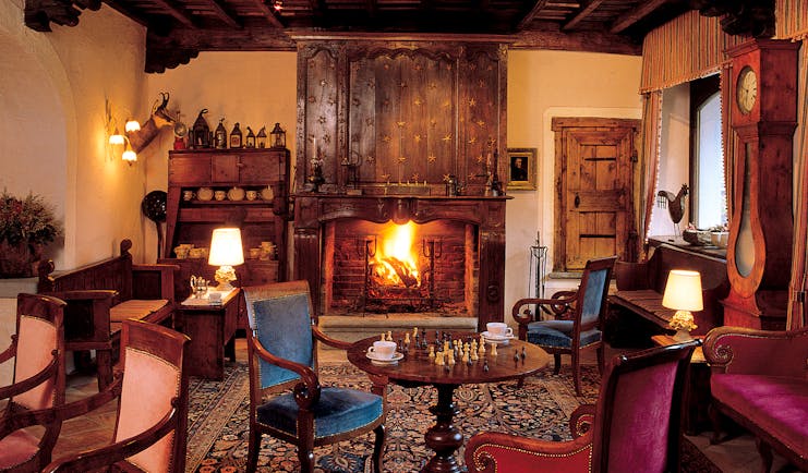 Cosy indoor lounge area with fire place, arm chairs, chess board on the table and old fashioned wooden deocrations