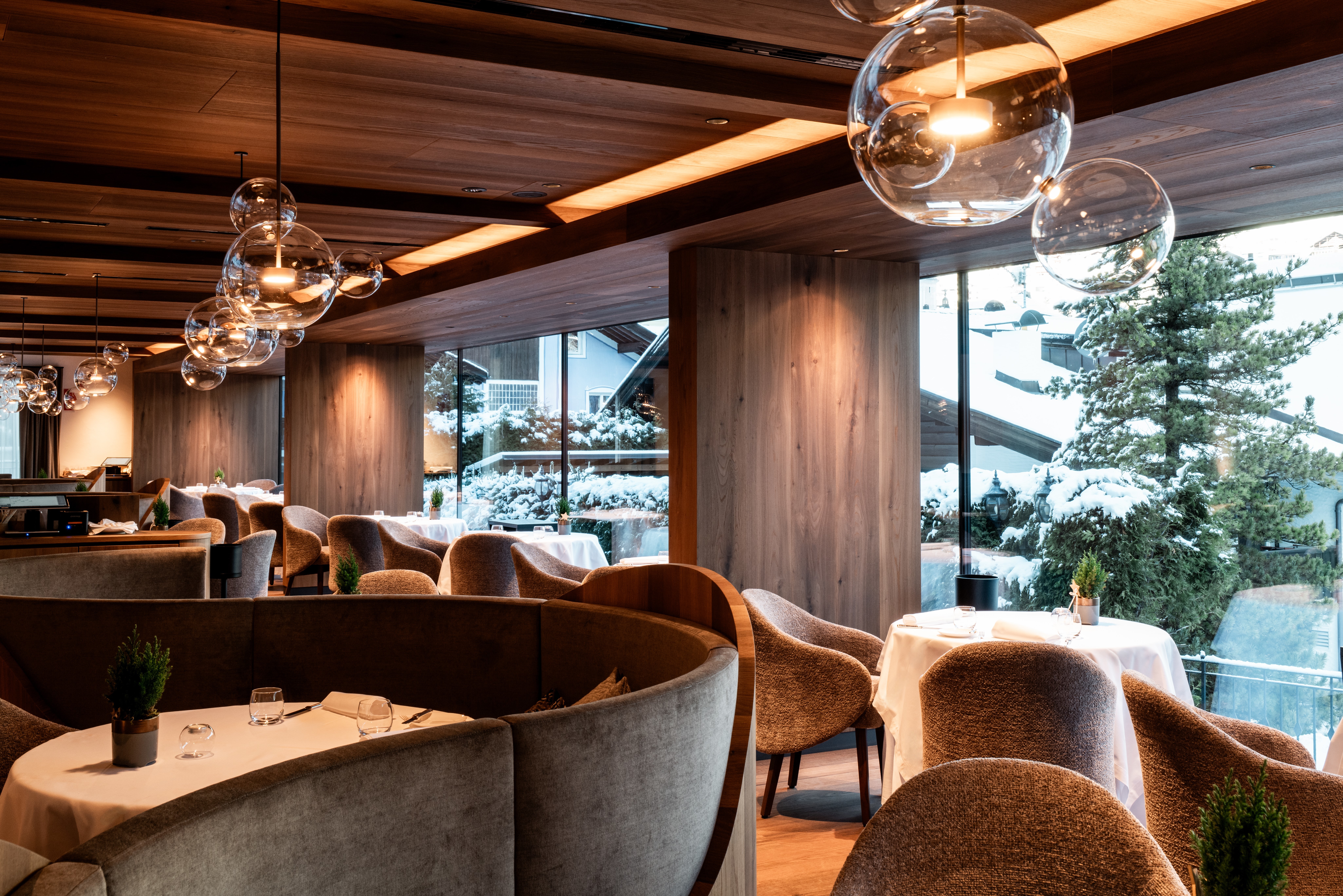 Garden Grodnerhof restaurant with curved, stylish modern furnishings, and floor-to-ceiling windows looking out onto the snow-covered mountainside