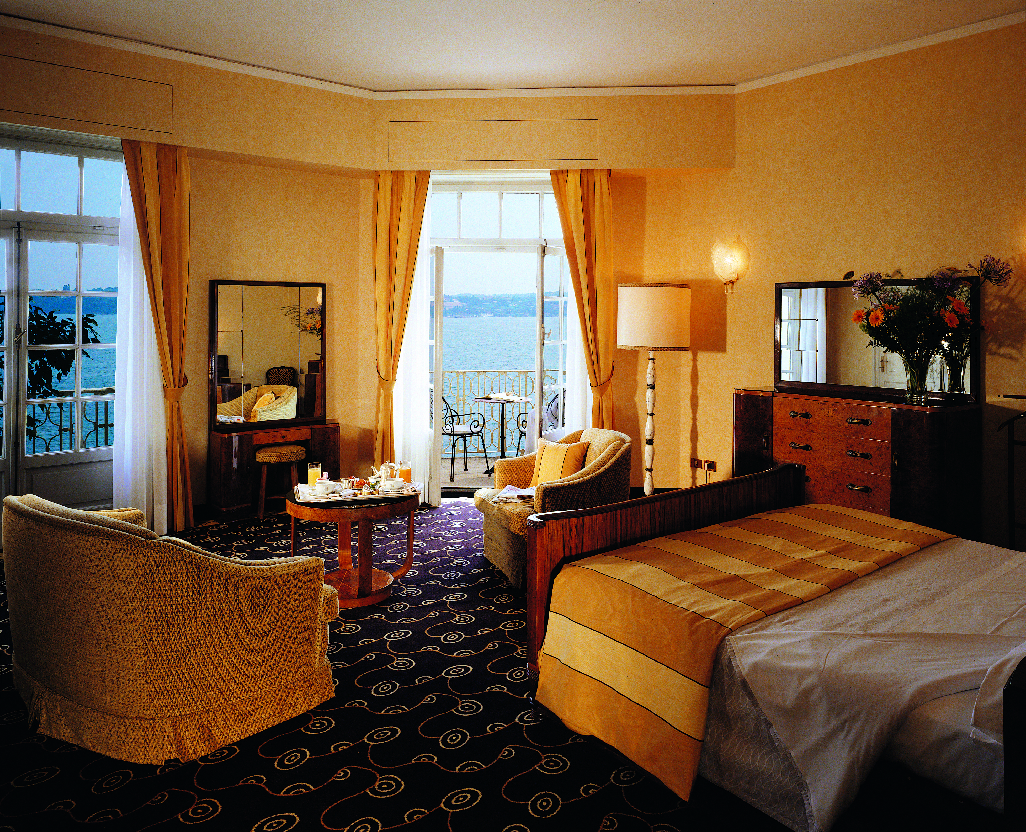 Grand Hotel Gardone Churchill suite with an orange and white colour scheme with a big double bed and large doors opening up onto a terrace balcony looking over the lake