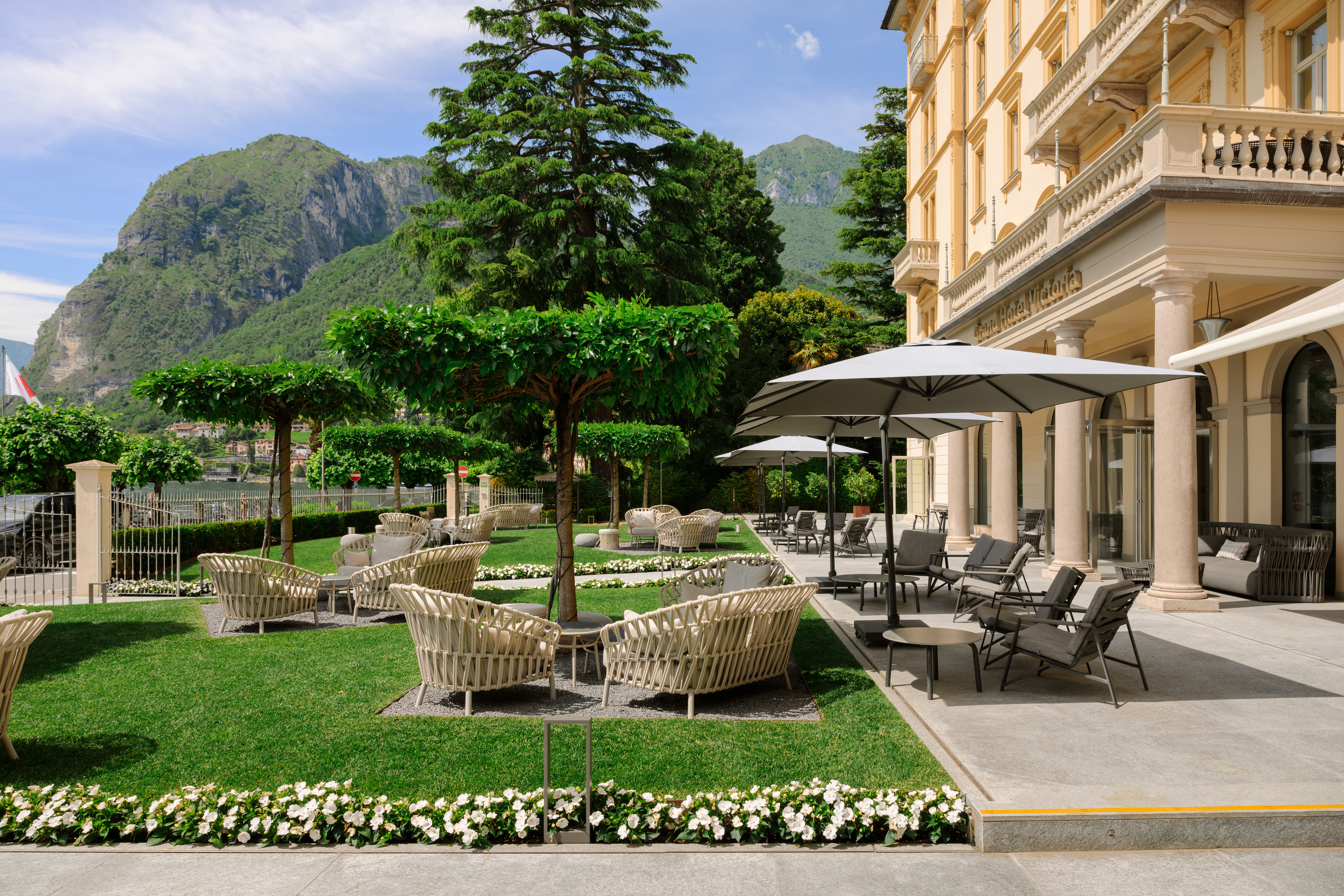 Grand Hotel Victoria Concept & Spa outside seating under manicured trees with lakeside mountains in view