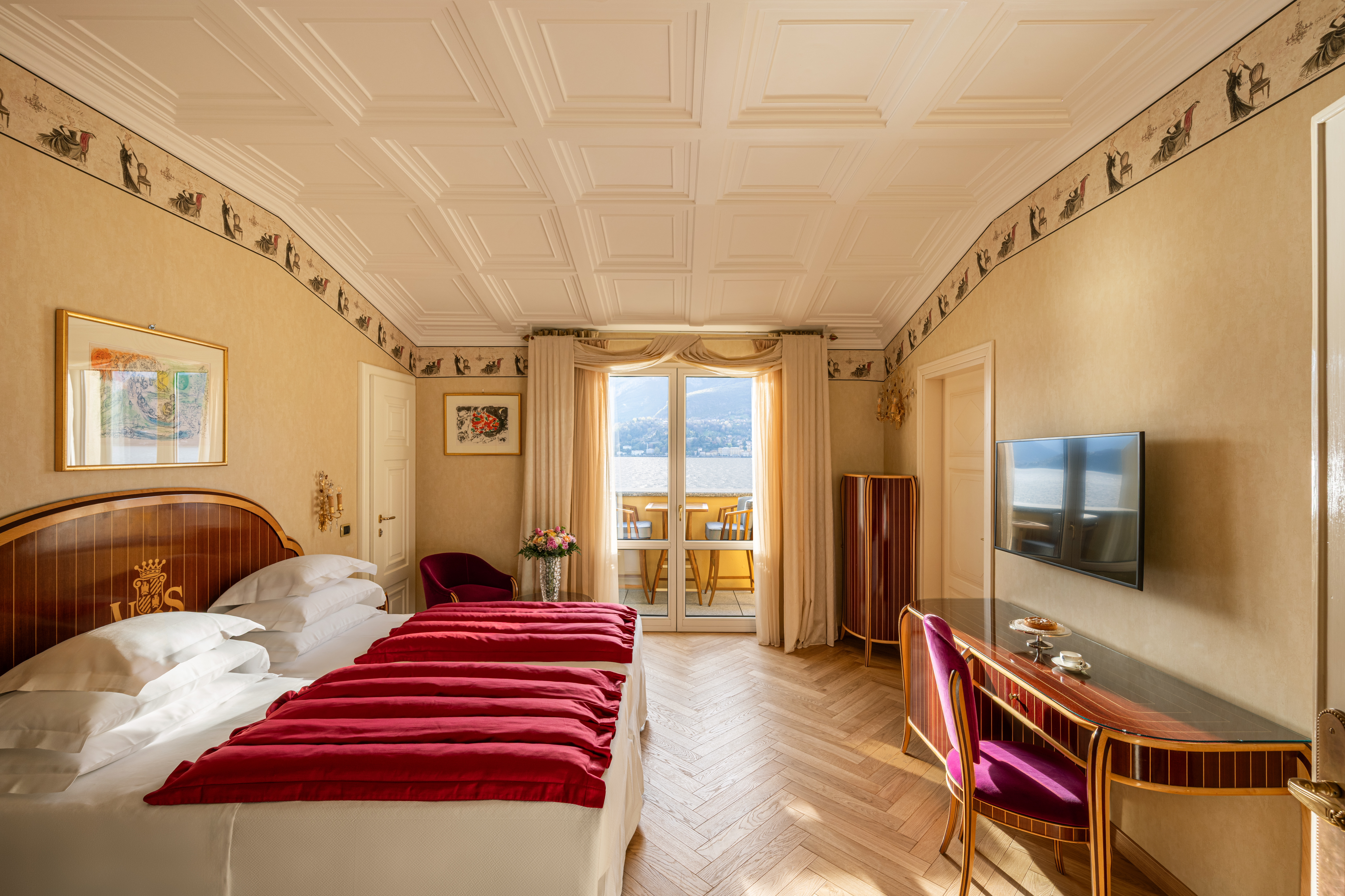 Grand Hotel Villa Serbelloni Classic Lake View Room with two single beds with red covers, sloping beamed ceiling, desk, and double doors opening onto a small lakeview terrace