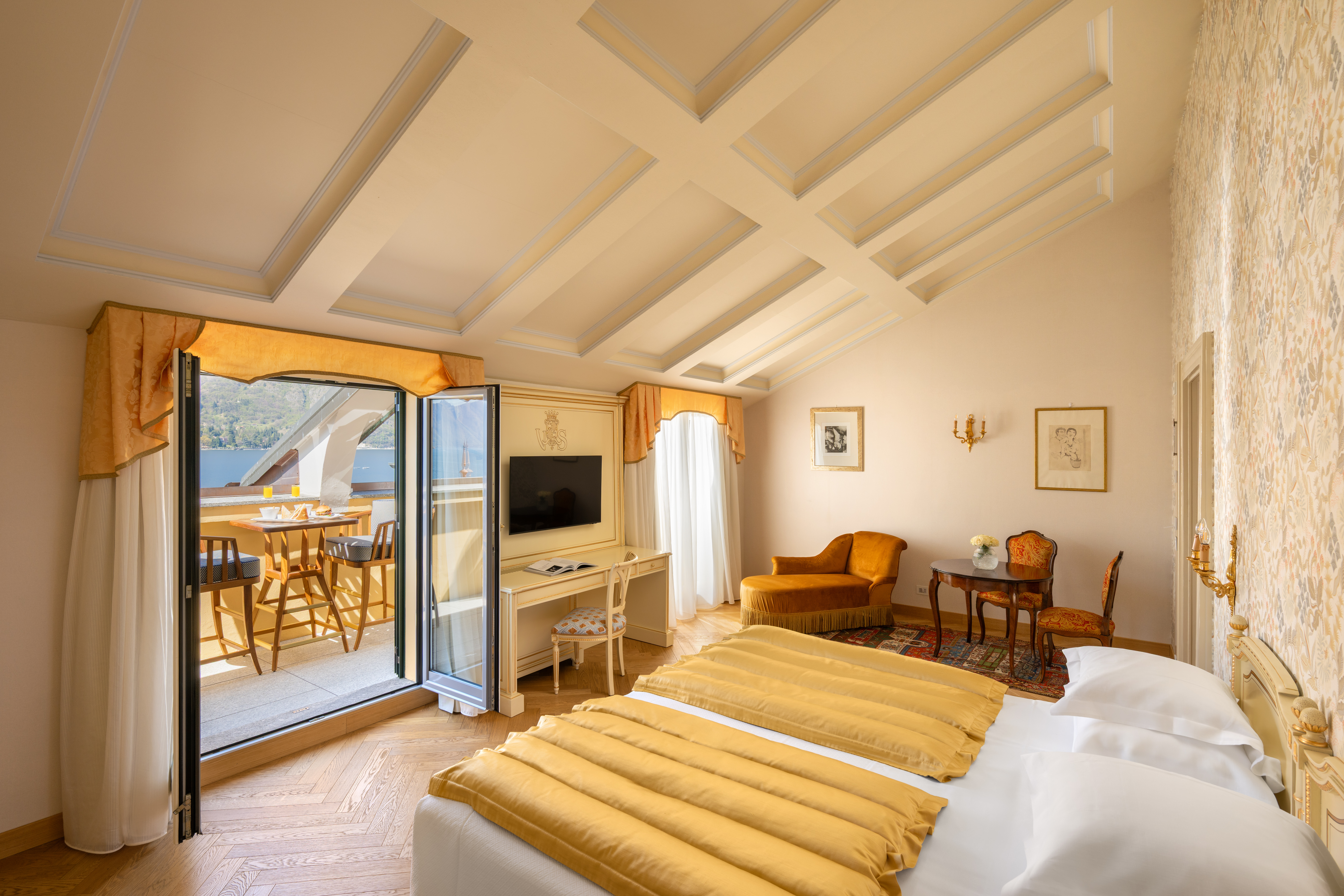 Grand Hotel Villa Serbelloni Deluxe Lake View room with two single beds with yellow covers, sloping beamed ceiling, and two sets of double doors opening onto a lake view terrace