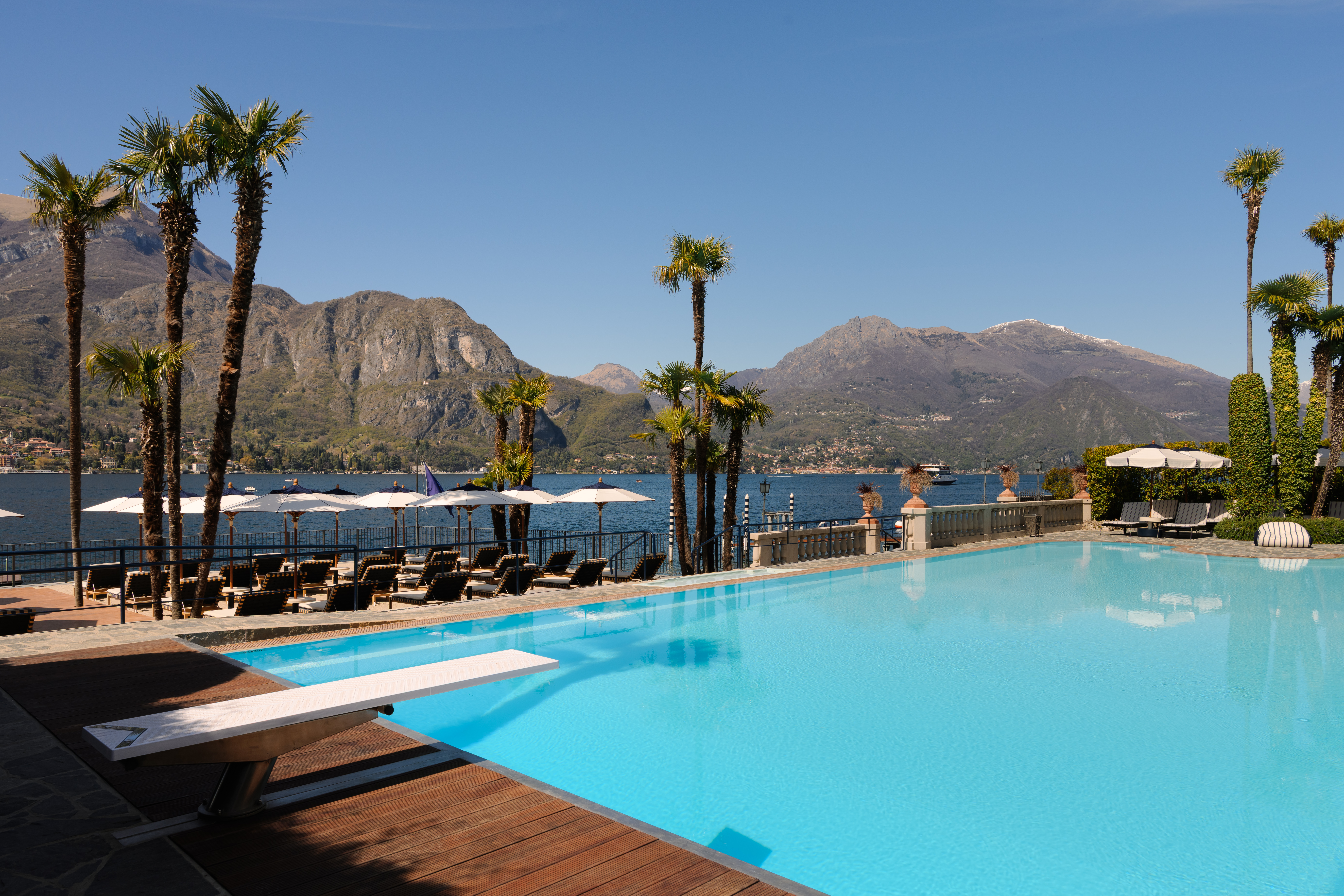 Grand Hotel Villa Serbelloni outdoor swimming pool, with wooden deck, diving board, bright blue water, and lake views