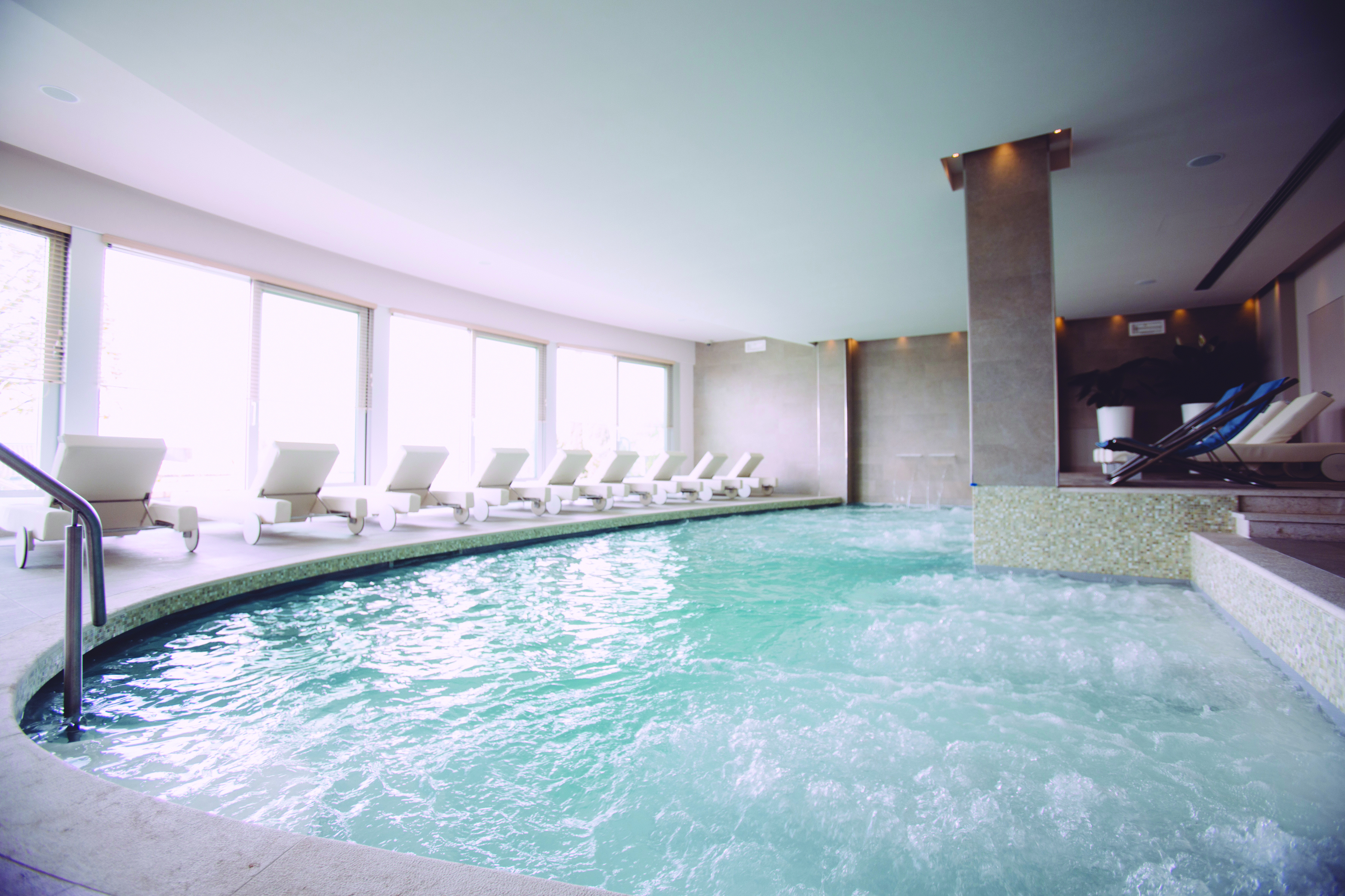 Hotel Olivi indoor pool with jacuzzi area, white sunbeds laid out around the pool 
